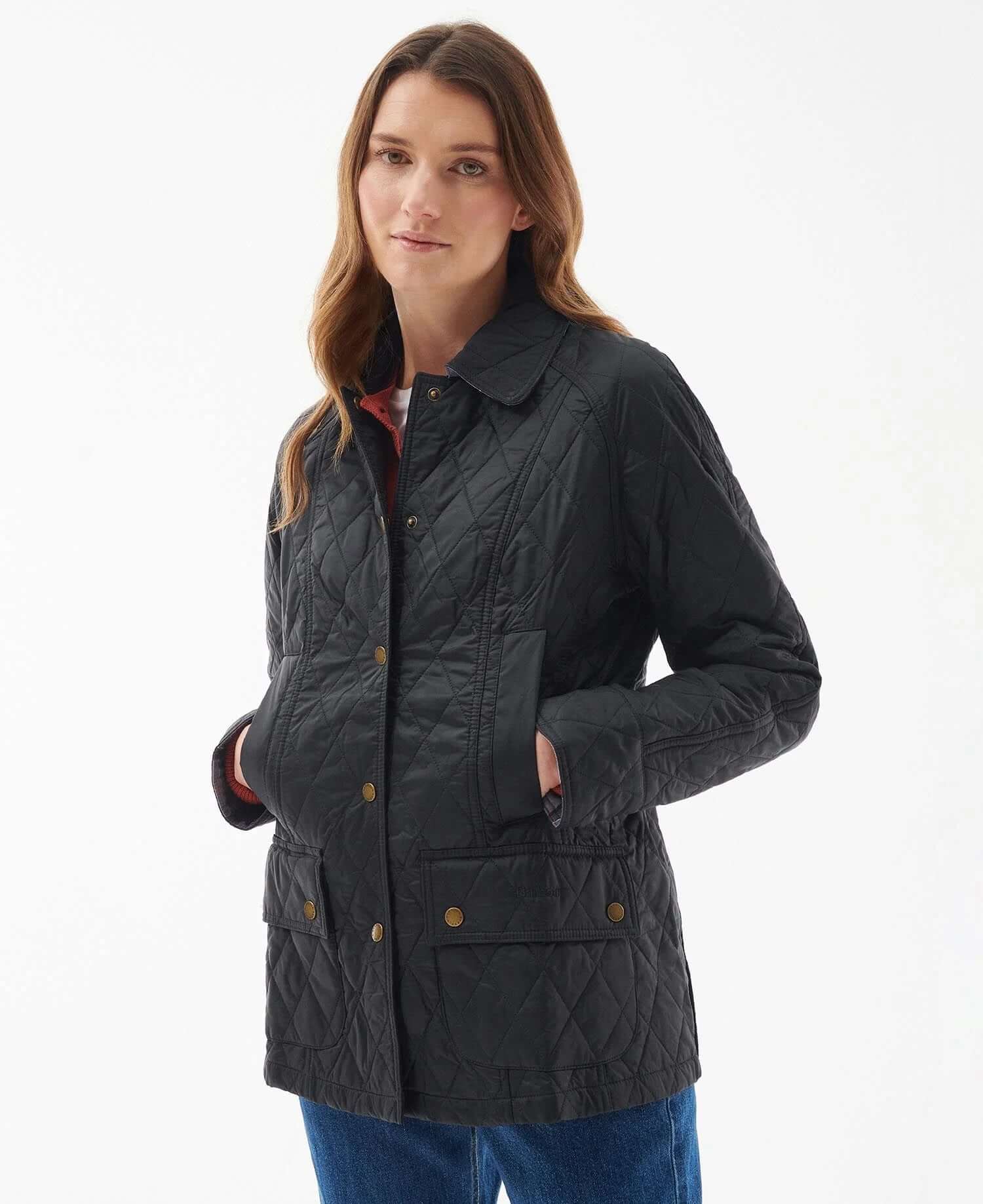 Woman wearing a black quilted jacket with front pockets and brass button details