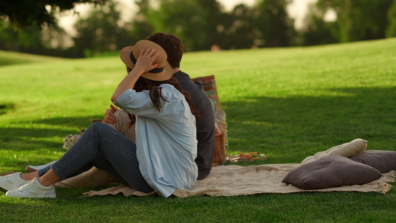 A couple sits together on a blanket in a grassy park, enjoying a peaceful picnic