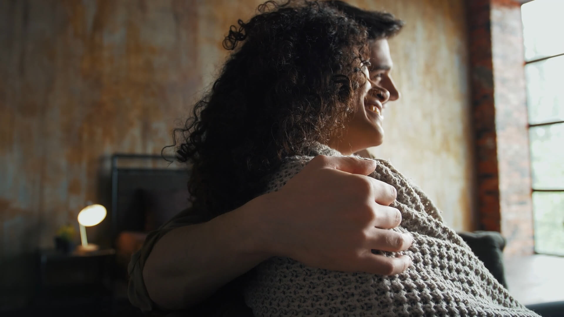 A couple sitting close together on a cozy couch, one person embracing the other from behind