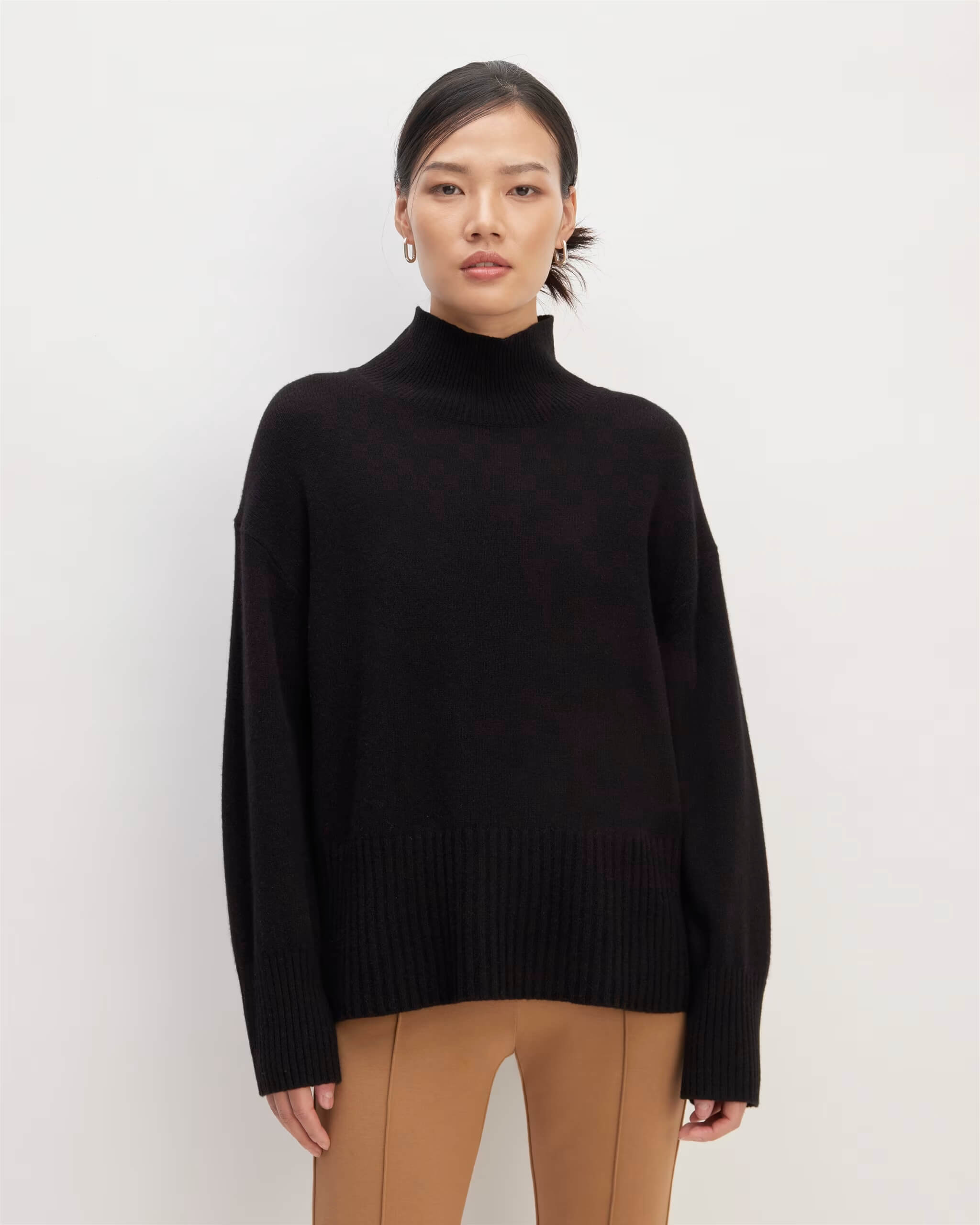 Woman wearing a black oversized cashmere turtleneck sweater paired with camel-colored pants