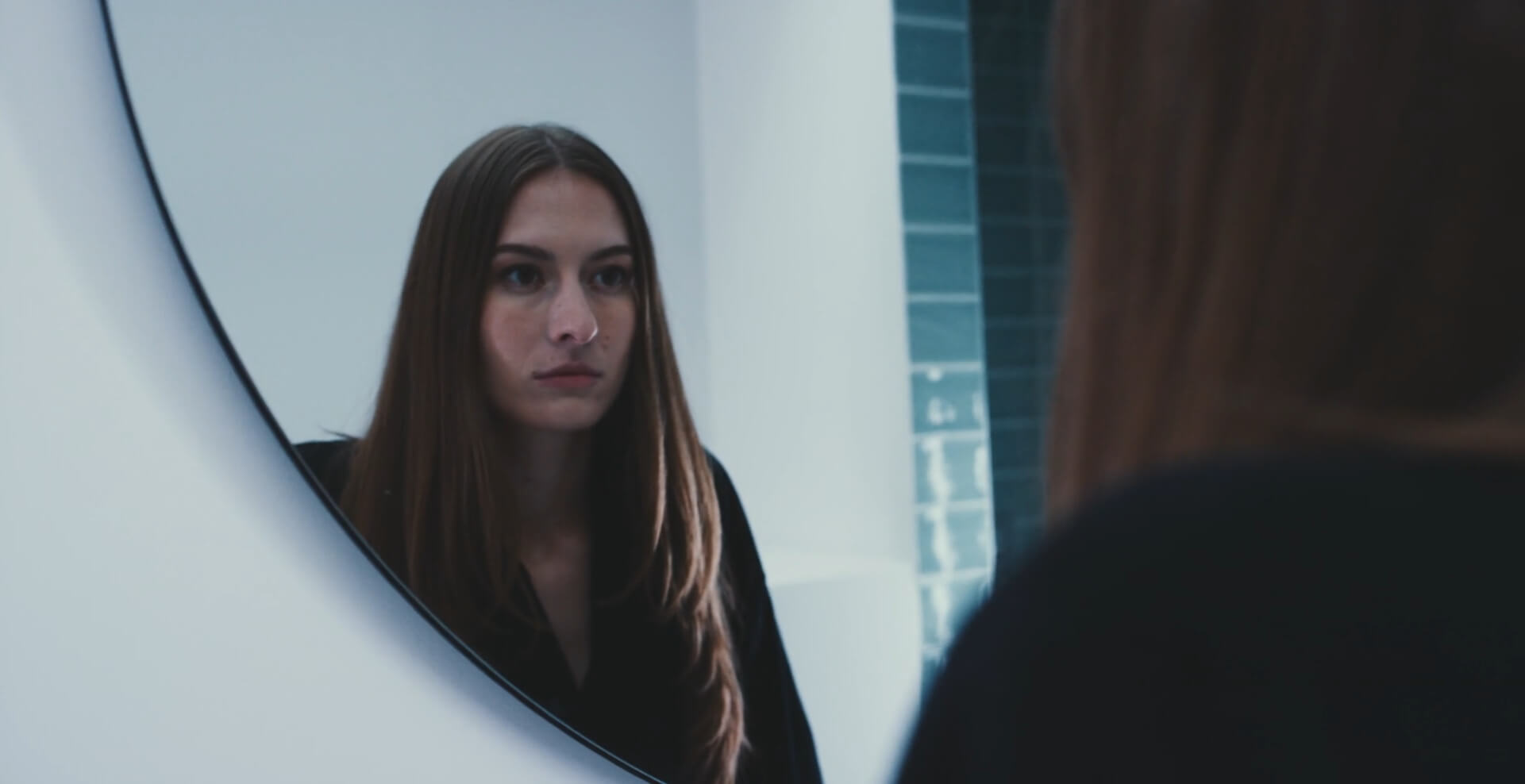 A woman looking at her reflection in a round mirror