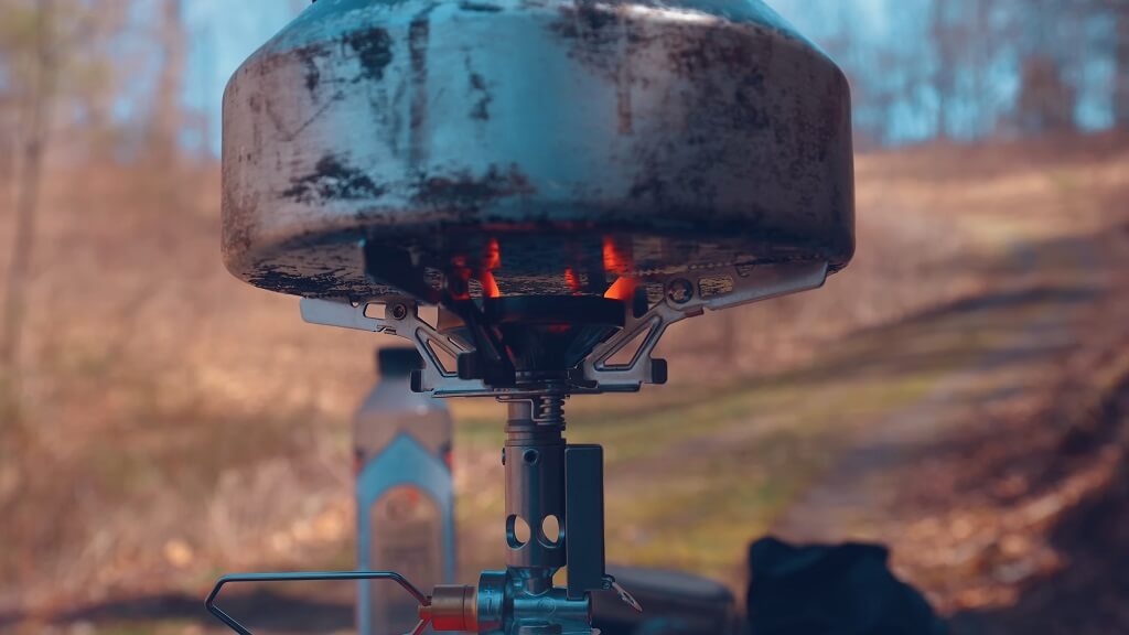 A close-up of a camping stove heating a pot, with flames visible beneath the pot