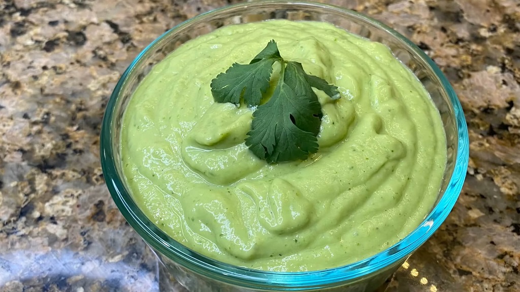 A glass bowl of creamy avocado dip on a granite countertop