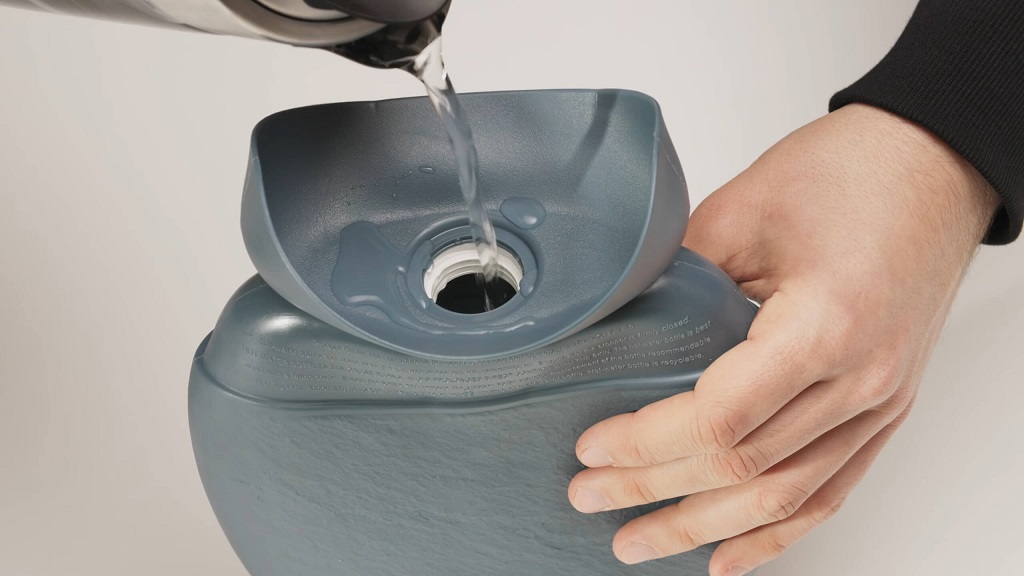 A gray Fashy hot water bottle being filled with hot water from a kettle