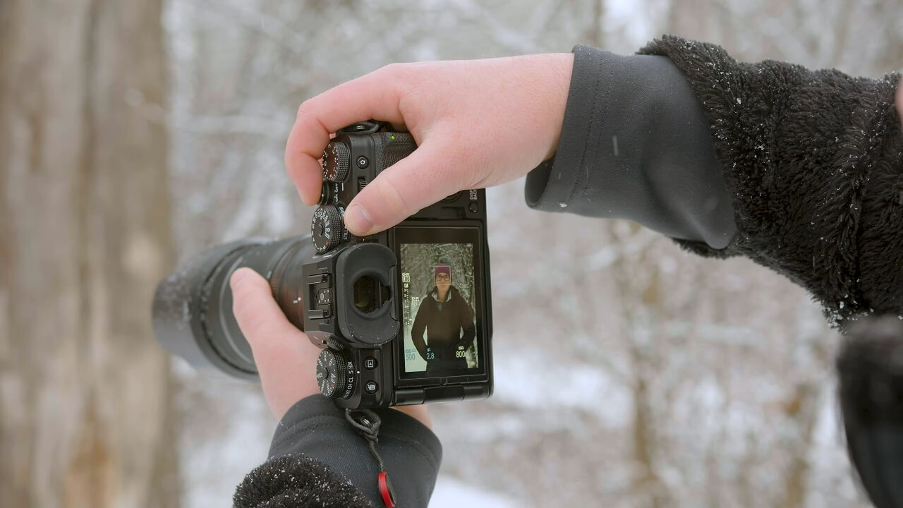 A photographer adjusting their camera settings in a snowy forest