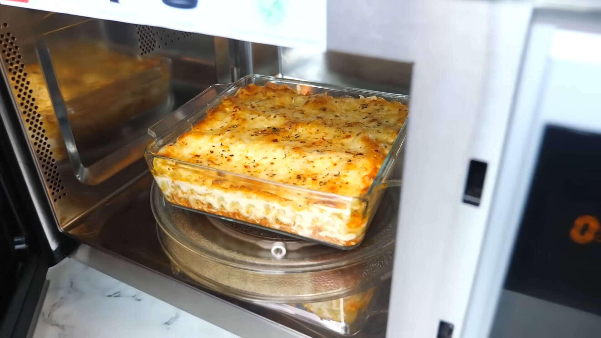 A bowl next to lasagna in the microwave