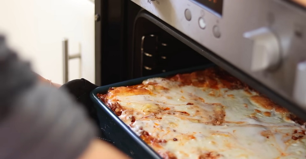 A woman is taking a lasagna tray out of the oven