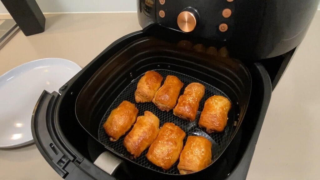 An air fryer basket containing perfectly reheated sausage rolls