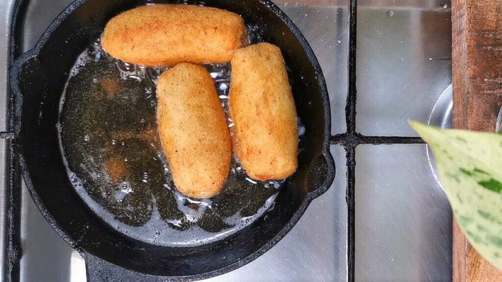 A skillet on a stovetop frying sausage rolls in oil