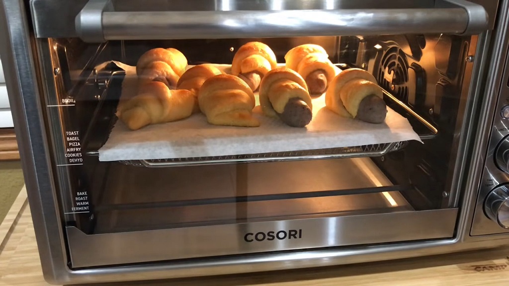 A toaster oven with freshly reheated sausage rolls on a baking tray