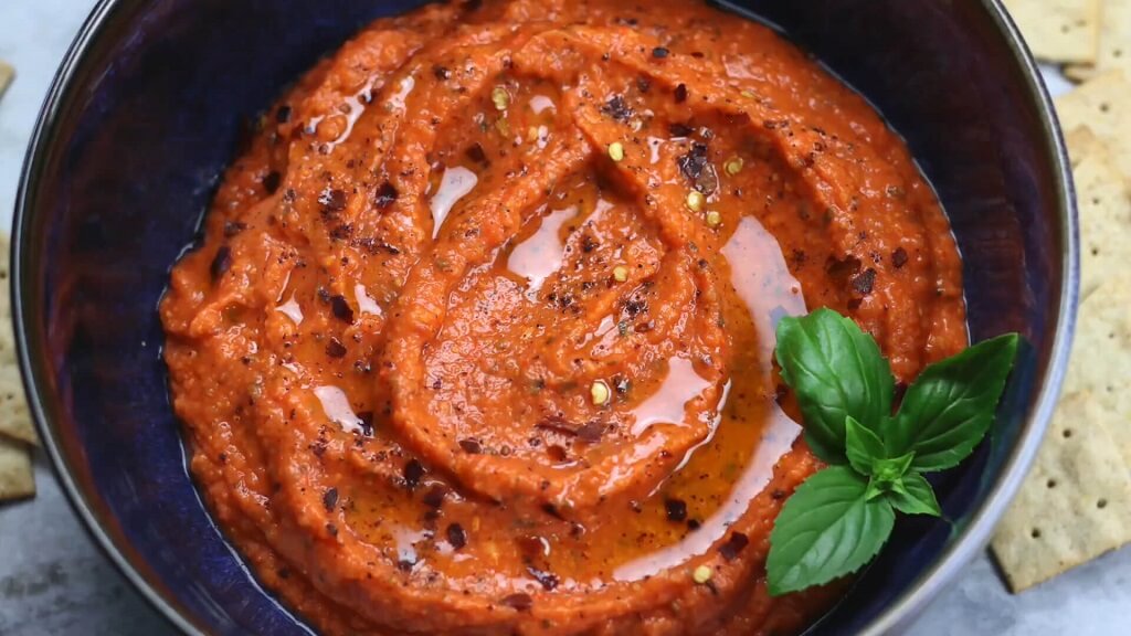 A bowl of roasted red pepper dip with basil garnish