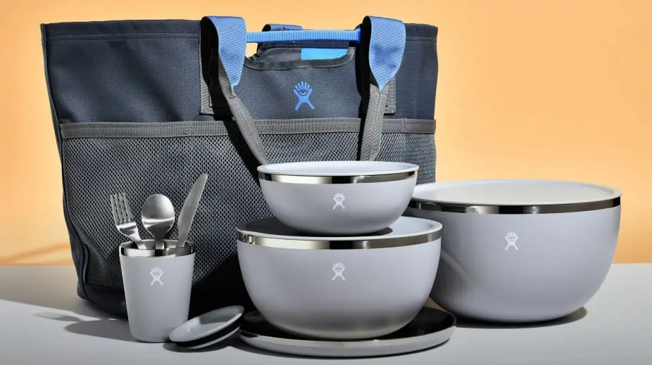 A set of gray insulated serving bowls with lids, accompanied by utensils and a blue-handled carry bag