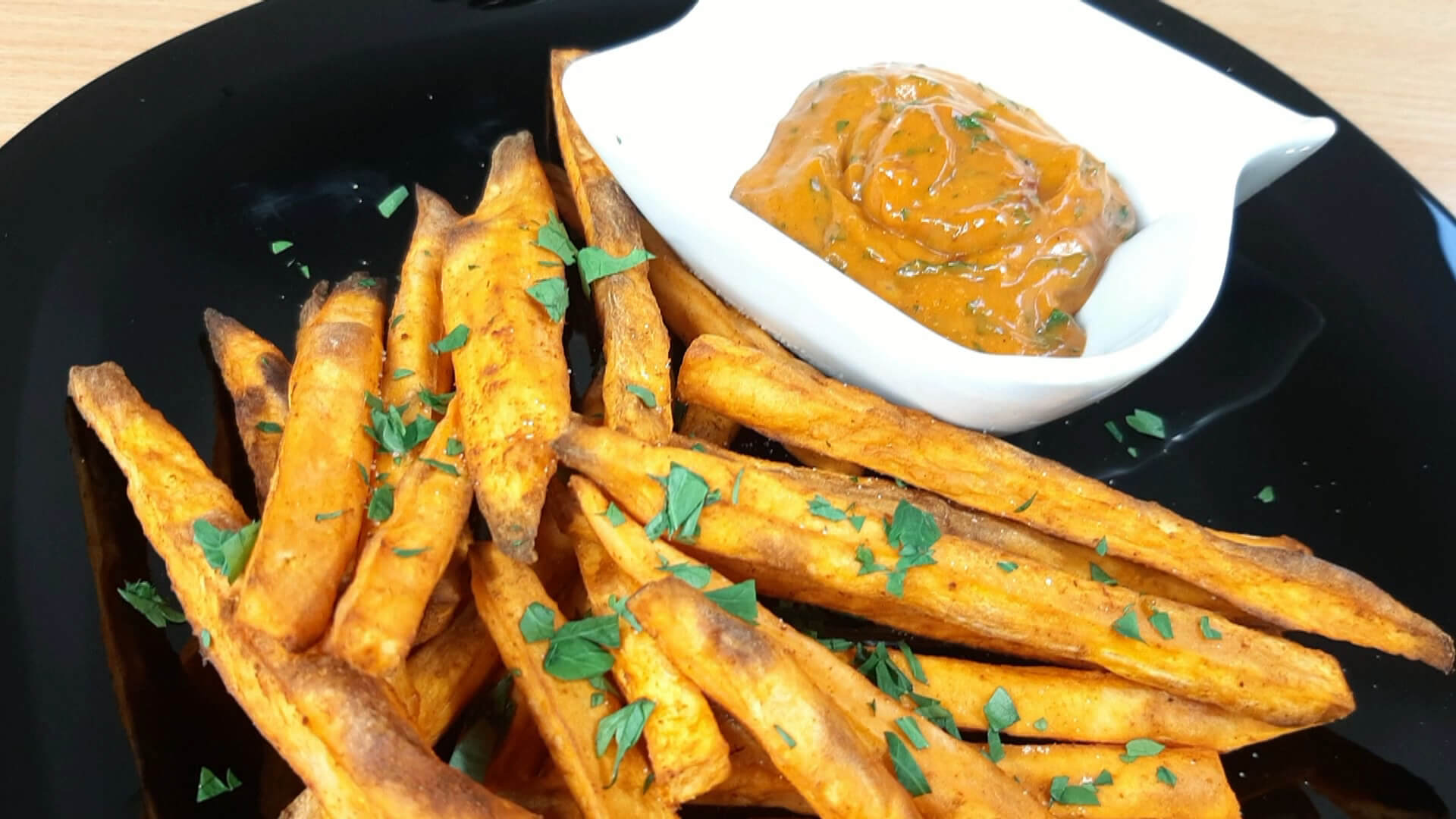  A small dish of orange-hued sweet potato curry dip next to a plate of sweet potato fries