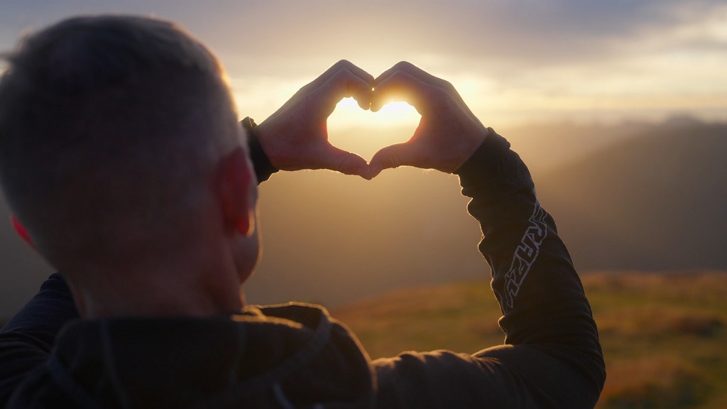 A guy forming a heart shape with his hands during sunrise