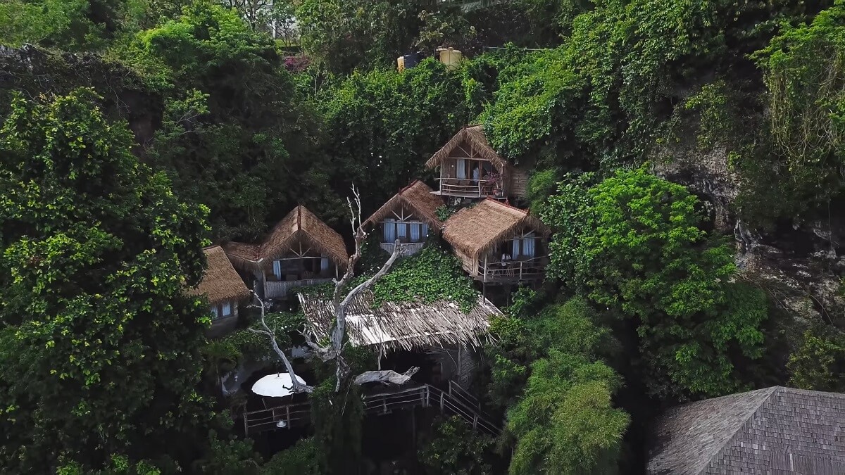 A cluster of traditional thatched-roof huts nestled in lush green jungle on a hillside in Indonesia