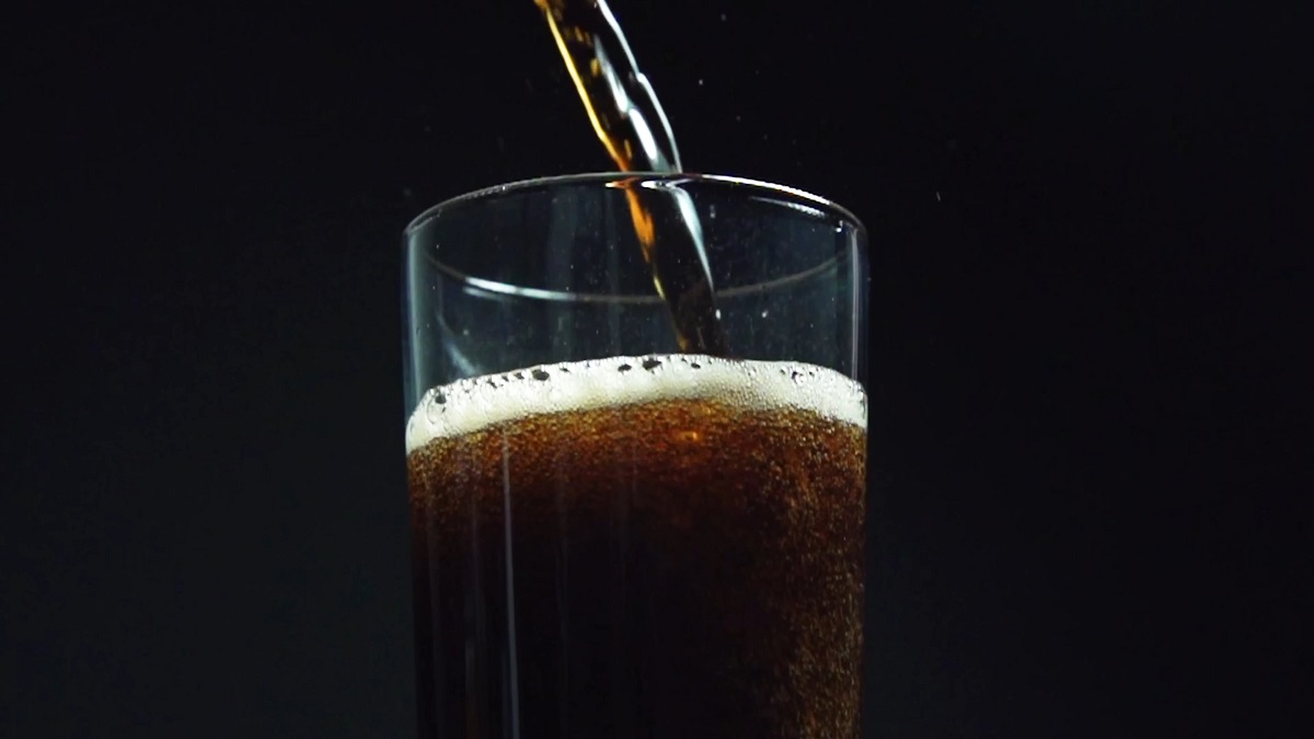 A dark, fizzy cola being poured into a glass against a black background, with bubbles forming at the top