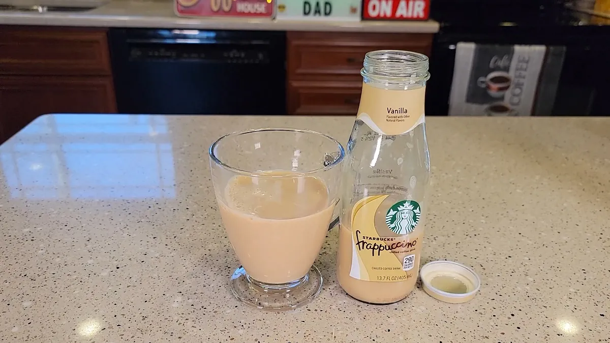 A glass of poured Starbucks Vanilla Frappuccino sits next to an open