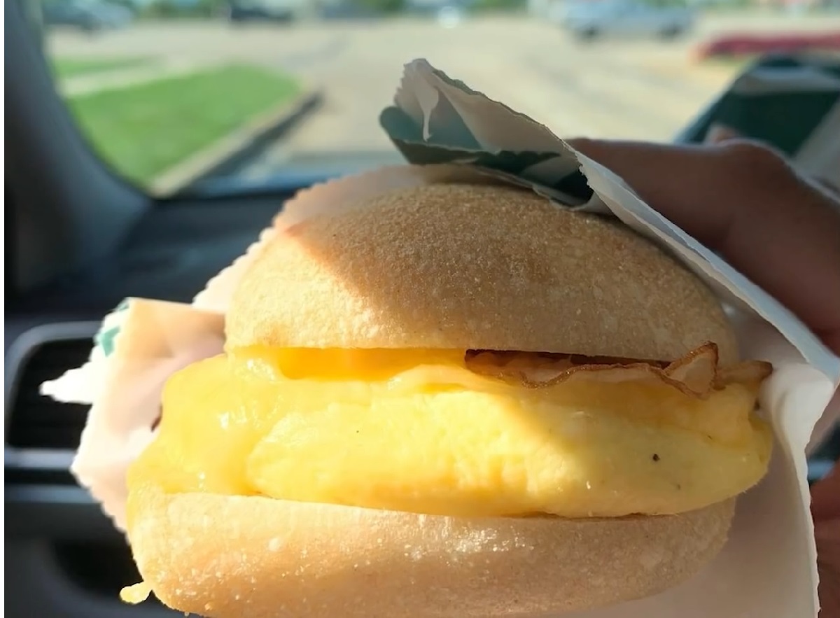 A bacon, gouda, and egg sandwich with fluffy eggs and toasted bread held in a car