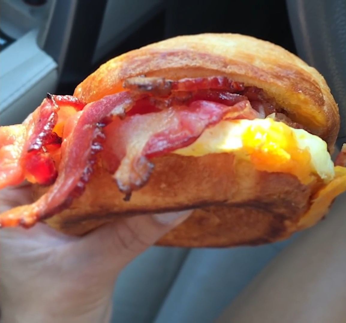 A double-smoked bacon, cheddar, and egg sandwich with crispy bacon and melted cheese in a car